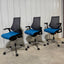 Set of three office chairs with blue seats and black frames on a metal stand against a white wall.